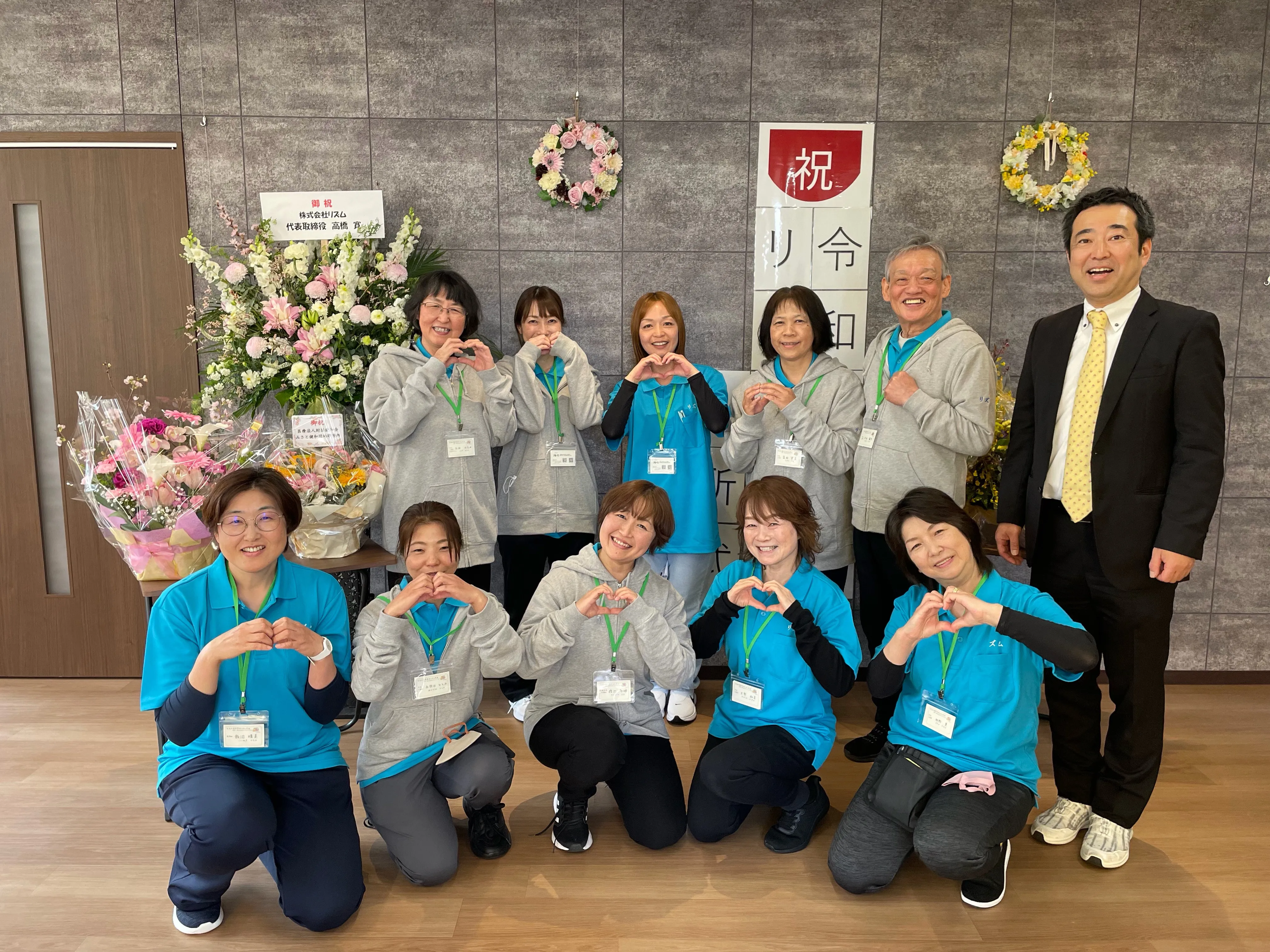 開所式で集まったリズム彦成のスタッフ。両手でハートの形をつくって笑顔を見せている